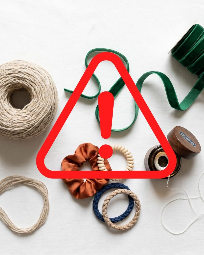 cat hazards A 1:1 square flat lay photograph by Solstice Cats on textured linen fabric, detailing common linear foreign body hazards: bright blue ribbon, multicolored hair ties, dental floss, yarn, and sewing thread with a needle. A bold red triangular warning symbol is placed over the center.